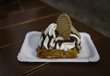 Üzerine yumuşak servis dondurması serpiştirilmiş, çikolata sosu serpiştirilmiş, waffle kurabiyesi ve kremayla süslenmiş, tatlı aşığı için mükemmel bir waffle.