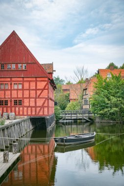 Geleneksel Danimarka mimarisini yansıtan huzurlu bir kanal kenarındaki kırmızı kereste evi. Bereketli yeşillik ve sakin sularla çevrili arka planda su değirmeni olan bu sakin sahne