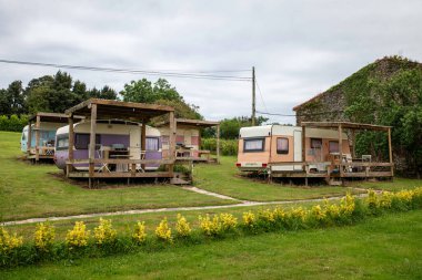 Ağaçlarla çevrili açık yeşil çayırlarda korunaklı güverteleri olan büyüleyici vintage kervanlar. Huzur ve kırsal konaklama seçenekleri arayan doğa aşıkları için sakin bir ortam oluşturur.