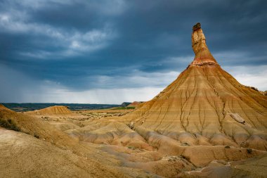 Bardenas Riales Doğal Parkı 'nın Bardenas Blanca bölgesinde Castildeterra kaya oluşumunun arka planı olarak kara bulutlar ve yağmur yağar.