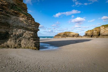 Playa de Katedrales 'in kayalık kayalık uçurumunun açık mavi gökyüzünün altındaki kumlu sahil boyunca uzanan muhteşem manzarası doğanın etkileyici jeolojik yapılarını gözler önüne seriyor.