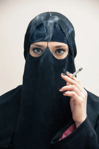 イスラム教徒のヒジャーブとイスラム教徒のドレスを身に着けている若い女性のクローズアップポートレート タバコと喫煙を保持 カメラを見て 目のメイクを示す目 白い背景に撮影スタジオ — ストック写真