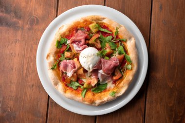 Delicious italian pizza with prosciutto crudo ham, rocket, tomato sauce, and mozzarella