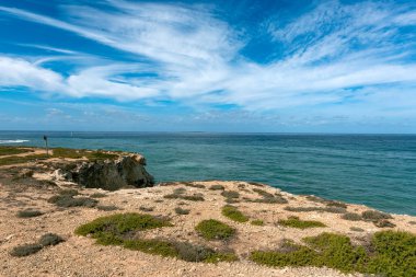 Deniz kenarındaki kayalardan, beyaz lekeli bulutlarla mavi gökyüzü manzarası