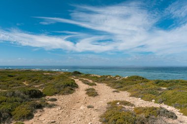 Deniz kenarındaki kayalardan, beyaz lekeli bulutlarla mavi gökyüzü manzarası