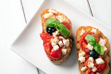 Bir tepsi lezzetli caprese bruschette, mozarella, domates, fesleğen, siyah zeytin, kekik ve zeytinyağlı tipik İtalyan aperatifleri.