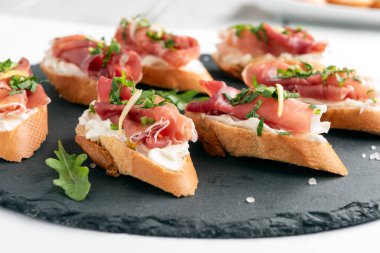 Peynir kremalı, roketli ve jambonlu lezzetli crostini tabağı, İtalyan aperatifi, Avrupa yemekleri.