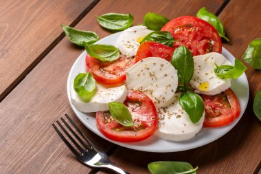 Tahta masada taze domatesli caprese salatası, fesleğen yaprağı ve mozzarella.