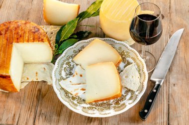 Tahta zemin üzerinde şarap kadehi olan sert peynir tabağı.