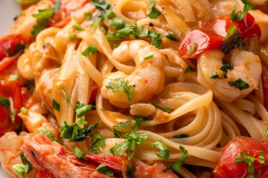 Siyah tahta bir masada beyaz tabakta deniz ürünleri ve karidesli makarna.