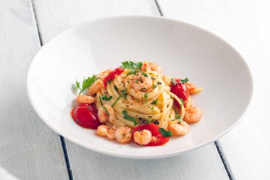 Maydanoz ve domatesle süslenmiş karidesli makarna.