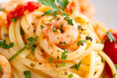 Maydanoz ve domatesle süslenmiş karidesli makarna.