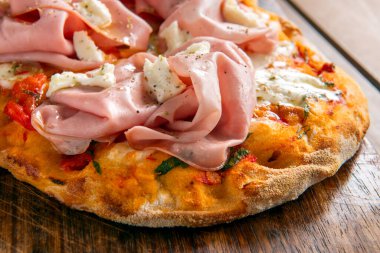 Yakın plan, üzerinde jambon dilimleri olan rustik pizzayı gösteriyor.