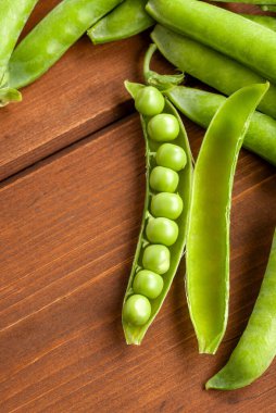 Açık kabuktaki taze bezelyeler tahtanın üzerinde dinleniyor.
