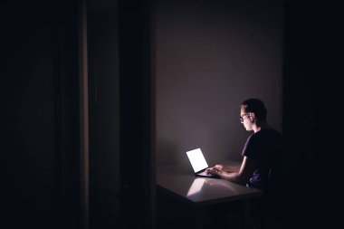 Karanlık ofis odasında dizüstü bilgisayarla gece işi. Genç adam defter bilgisayarı kullanıyor. Yazılımcı, programcı, hacker, serbest dijital editör ya da öğrenci. İşine odaklan. İşkolik fazla mesai yapıyor.