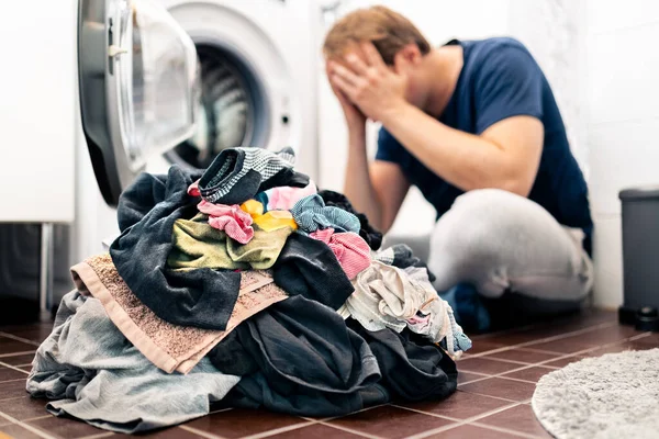 Tired and unhappy of laundry, washing clothes, house chores and housework. Sad man or overwhelmed young dad. Broken washing machine. Parenthood stress in family. Dirty home, problem in domestic work.