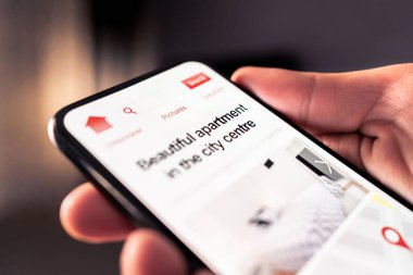 Rental property and apartment search with phone. House or vacation home for rent on website market. Internet research to find new condo lease or sale. Man using real estate marketplace in smartphone.