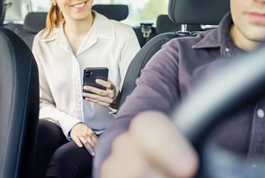 Taksi ya da araç paylaşımı yolcusu taksi parasını ödemek için telefonu kullanıyor. Cep telefonu ödemesi, bahşiş ya da inceleme. Mutlu müşteri ve şoför. Elinde cep telefonu olan bir kadın. Kız arkada gülümsüyor. Adam sürüyor..