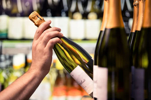 Sparkling wine from shelf of alcohol store. Bottle in hand. Liquor shop. Prosecco or champagne display in spirits market or supermarket. Man buying expensive drink. Choosing product from rack.