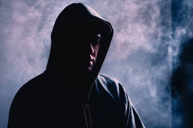 Gölgedeki suçlu. Gizli yüzlü, korkunç, şüpheli bir yabancı. Kara dumanlı sisli bir gangster silueti. Çete suçu ya da korku konsepti. Holigan, hırsız, hacker ya da kundakçı.