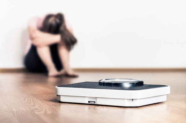 Weight loss and diet. Sad woman and scale. Stress of fail or being obese. Anorexia or bulimia concept. Frustrated teenager with eating disorder. Gaining body fat problem. Low confidence or trauma.