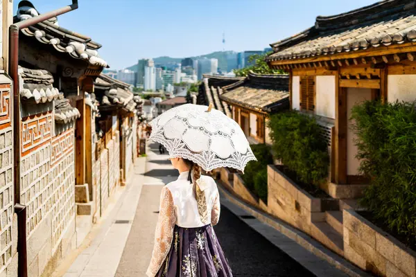 Güney Kore, Seul. Bukchon Hanok köyündeki Hanbok 'ta bir kadın. Geleneksel elbise ve kostüm giyen kız. Kore geleneği. Arka planda şehir silüeti var. Yazın ya da ilkbaharda seyahat et. Arka plan.