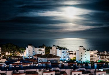 Ay ışığı, binalar ve deniz geceleri. İspanya 'nın Benalmadena tatil kasabasında ay ışığı. Şehrin yerleşim bölgesindeki tatil evleri ve daireleri. Avrupa 'da kiralık evler. Malaga yakınlarında sahil yolculuğu.