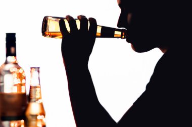 Alkol bağımlısı. Alkol sorunu ve taciz. Biralı bir adamın silueti. İçki tüketimi. Rehabilitasyon, detoks ya da iyileşme. Şarap şişesi masada. Beyaz arka plan. Karanlıktaki sarhoş genç alkolik kişi.