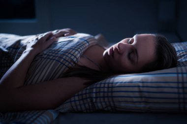 Geceleri yatakta uyuyan kadın. Melatoninden sonra güzel rüyalar. Derin REM. Karanlık yatak odasındaki kız. Yastık ve yorgan. Yüzü aydınlık. Rahat bir odada iyi istirahatler. Uyuyan kişi. Kabus, horlama ya da apne..