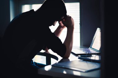 İş stresi. Endişeli yorgun bir adam. Dizüstü bilgisayarı olan üzgün bir ofis çalışanı. Hüsrana uğramış üniversite ya da üniversite öğrencisi. Endişeli kişinin karanlık silueti. Ev bilgisayarı. İşle ilgili kötü bir sorun.