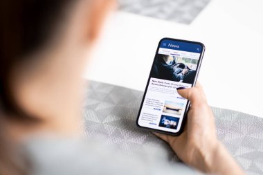 Telefondaki haberler. Basın açıklaması. Dijital medya okuyor. Cep telefonu ekranında çevrimiçi gazete modeli. Cep telefonu kullanan bir kadın. Akıllı telefondaki son başlıklar.