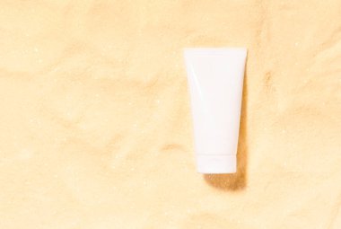 Sahte güneş kremi ya da losyon şişesi. Sarı kumdaki beyaz kozmetik tüplü yaz güneşi koruma şablonu sahnesi. Ürün sunumu veya paket reklamı.