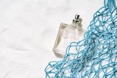 Parfüm. Mavi pamuk örgüsünün yakınındaki kumların üzerinde duran şeffaf parfüm şişesiyle yapılmış deniz notaları konsepti olan bir adam kokusu. Kopyalama alanı olan arkaplan.