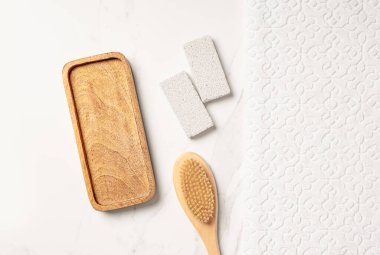 Boş ahşap tepsi, beyaz havlu, sünger taşı ve fırça fırçasıyla yapılmış düz bir vücut bakımı sunumu sahnesi.
