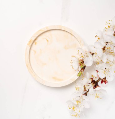 Güzellik kozmetik ürünleri sunumu bej mermer daire şekli ve kayısı ağacının çiçek açan dalından yapılmış düz bir maket sahnesi. Stüdyo fotoğrafçılık.