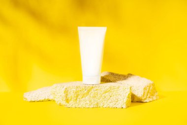Sarı zemin üzerinde kozmetik ürünleri sunumu için sünger taşlarının üzerine boş beyaz krem tüpü..