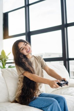 Duygusal kız online video oyunu konsolu oynuyor. Modern oturma odasında televizyon karşısında oturuyor. Dikey fotoğrafçılık.