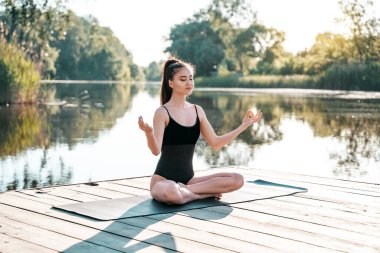 Yoga yapan güzel bir Yogi kadını, gözleri kapalı, nehir kıyısındaki Padmasana iskelesinde nilüfer pozisyonunda oturuyor. Sabah atmosferi.