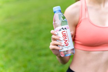 Illustrative editorial of famous bottled French Evian water in female hand. Evian is a French brand of premium water. POLTAVA, UKRAINE - June 08, 2023. clipart