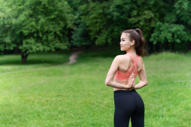 Sabah yogası dışarıda egzersiz yapıyor. Güzel Asyalı kız, parkta temiz havada ellerini kürek kemiklerinin arkasında birleştirerek pilates yapıyor..