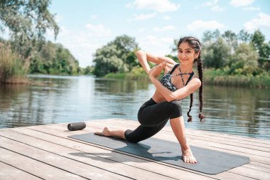 Güzel Hintli kadın yoga yapıyor ve nehir kenarındaki ahşap iskelede pilates yapıyor..