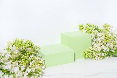 Kozmetik cilt bakımı sunum sahnesi yeşil podyumlar ve beyaz arka planda leylak çiçekleri ile yapılır.