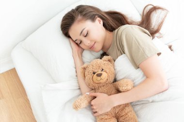 Beyaz çarşaflar içinde uyuyan güzel bir kadının portresi. Yatak odasında oyuncak ayıyla sarılıp uyuyor. Güzel bir hafta sonu ve yalnızlık konsepti.. 