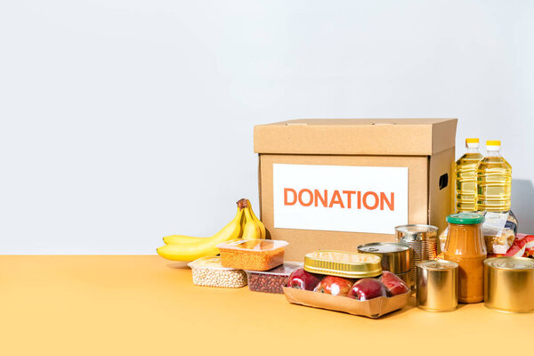 Коробка для пожертвований с различными продуктами на столе с копировальным местом. Гуманитарная помощь людям, оказавшимся в трудной ситуации.