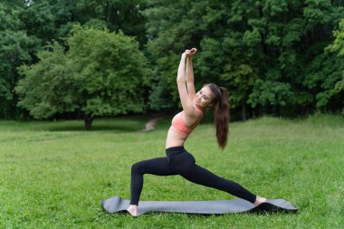 Doğanın enerjisiyle parkta sabah egzersizi yapan genç bir kadın.