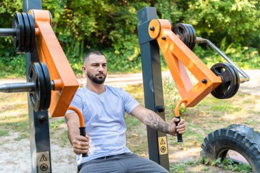 Açık spor salonu. Yakışıklı sakallı adam sokak egzersiz aletlerinde çalışıyor..