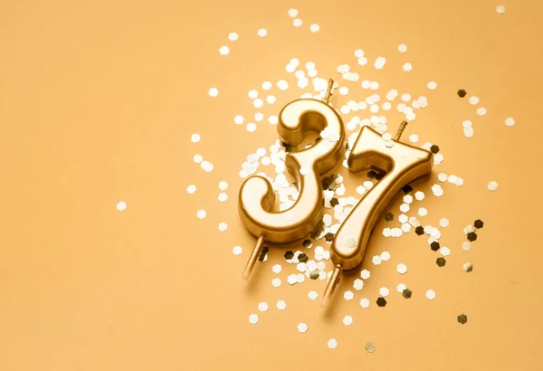 37 years birthday celebration festive background made with golden candle in the form of number Thirty seven lying on sparkles. Universal holiday banner with copy space.