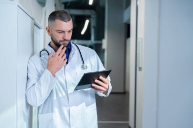 Karizmatik ve ilgili doktor, hastanın tıbbi bakımında profesyonellik ve bakım sergileyerek dijital tablette tıbbi geçmişini dikkatlice incelerken görülüyor..