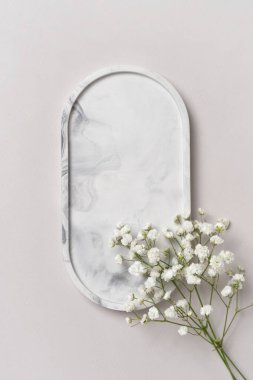 Markanızın minimalist tarzını vurgulayan yumuşak mermer oval tepsiye karşı narin beyaz çiçeklerin sunum sahnesi. Kozmetik, cilt bakımı ya da lüks ürünler için ideal.