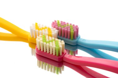 Yansıtıcı yüzeyde pembe, sarı ve mavi saplı üç renkli diş fırçası..